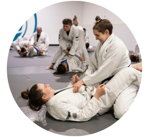 Two Jiu-jitsu students practice a choke hold on the ground while an instructor assists