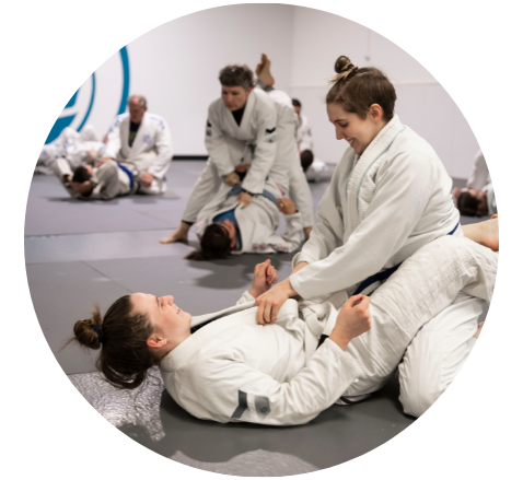 Two Jiu-jitsu students practice a choke hold on the ground while an instructor assists