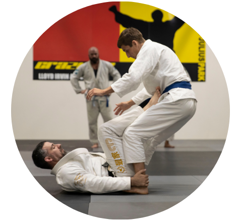 Two Jiu-jitsu students practice a choke hold on the ground while an instructor assists